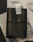 Black leather notebook with a silver clip on a textured surface