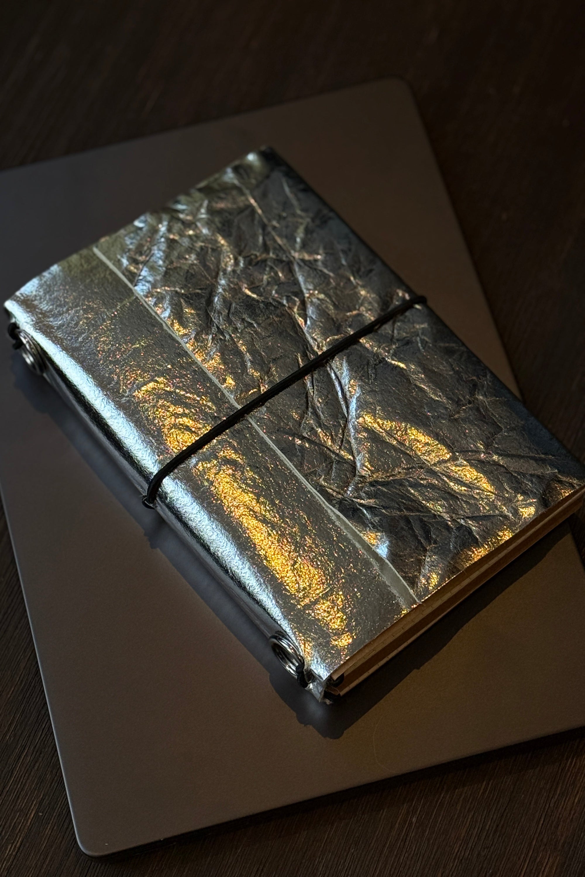 Silver metallic notebook with a black strap on a dark surface