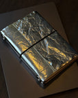 Silver metallic notebook with a black strap on a dark surface